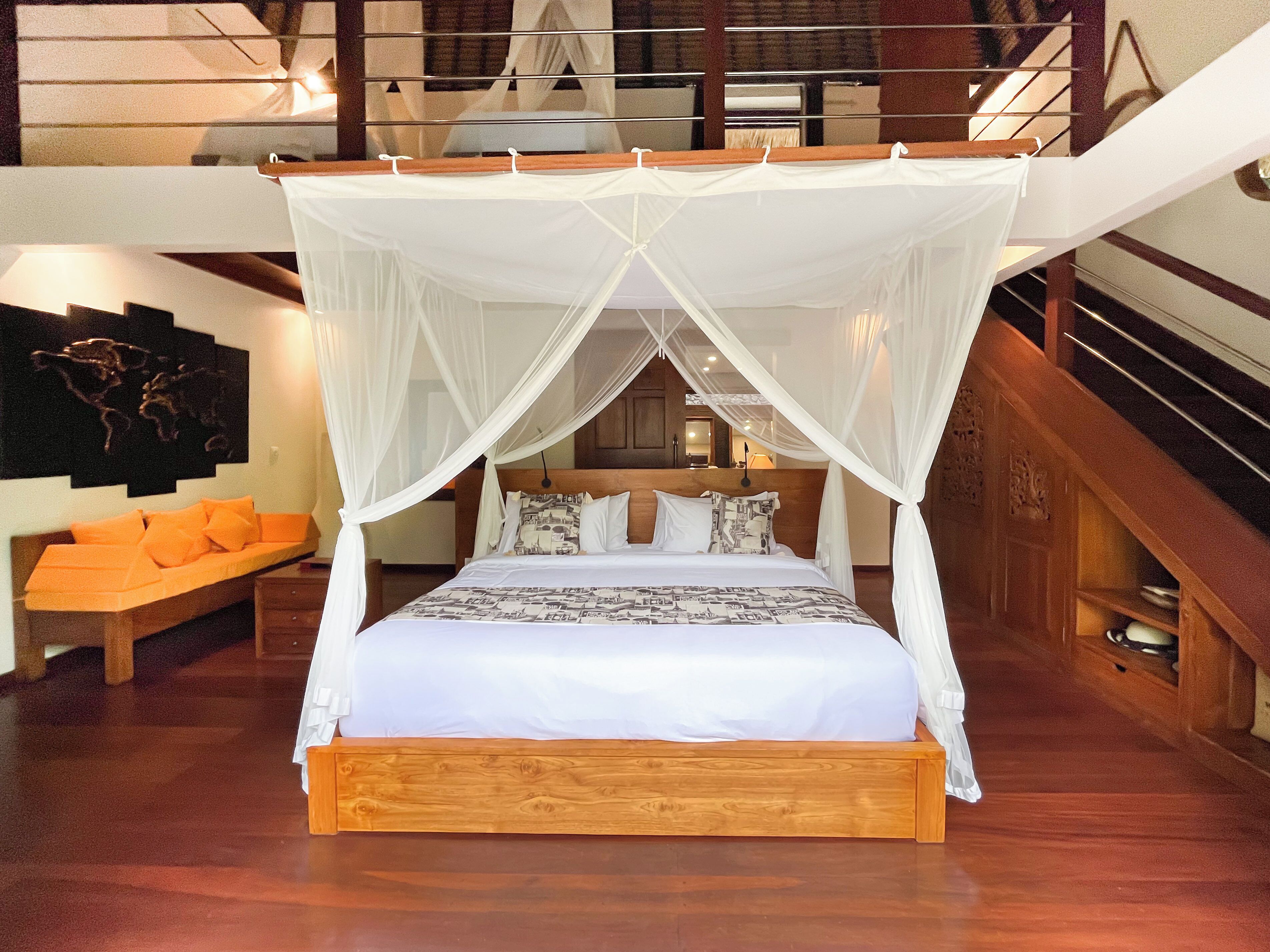 A bedroom with a four-poster canopy bed, wooden headboard, and a bench with orange cushions.