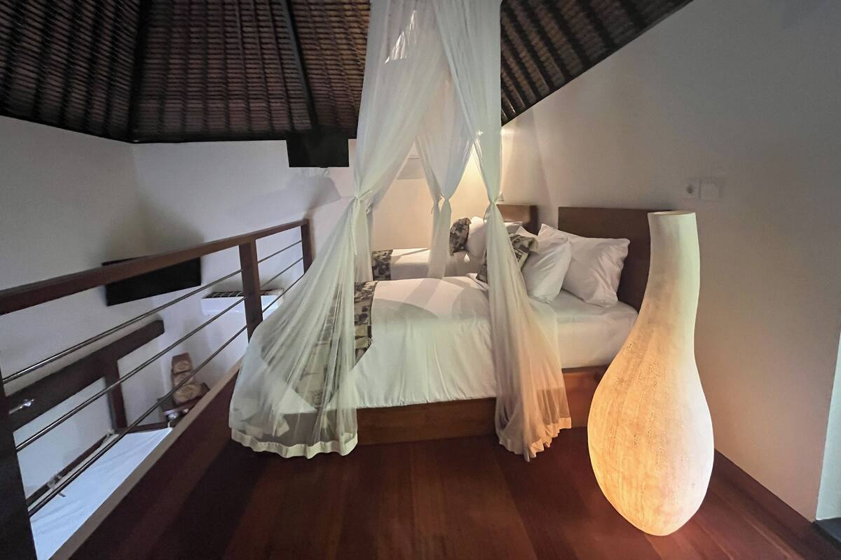 Een slaapkamer met hemelbed, een grote vaas en een trap.