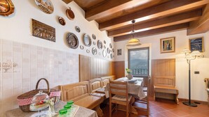 Une cuisine avec des bancs en bois, une table à manger avec un panier et un présentoir à gâteaux, et une vue par la fenêtre.
