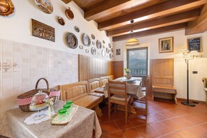 A kitchen with wooden benches, a dining table with a basket and a cake stand, and a view through a window.