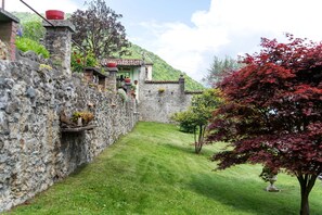 Un mur de pierre, un petit jardin et un bâtiment avec un toit recouvert de tuiles.