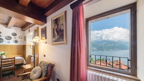 Une pièce avec un plafond en bois, une fenêtre donnant sur les montagnes et l’eau, une chaise avec un coussin, une table et une lampe.