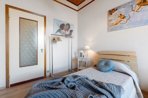 Un dormitorio con cama, mesita de noche, lámpara, puerta con vidrio esmerilado y un cuadro en la pared.