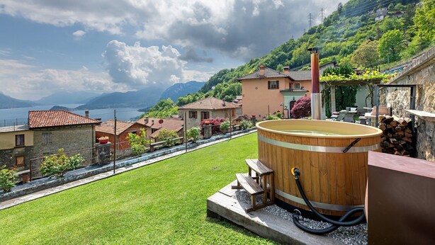 A wooden hot tub on a patio with a view of a lake and mountains.