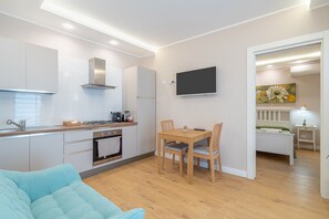 A modern kitchen with white cabinets, a flat-screen TV, and a dining area with a wooden table and chairs.