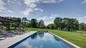 En rektangulär swimmingpool med ett trädäck i förgrunden, omgiven av en gräsyta och träd.