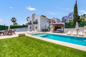 Una casa moderna amb piscina, mobiliari d'exterior i un jardí ben cuidat.