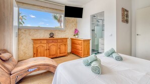 A bedroom with a bed, wooden furniture, a TV, a window with a view, and a bathroom with a glass door. - Villa 'Farau' with Sea View, Wi-Fi and Air Conditioning (Calpe)