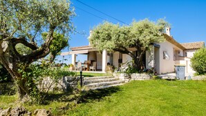 Una casa con una escalera de piedra que conduce a un porche cubierto, un árbol grande en primer plano y un cielo azul despejado.