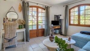 Una habitación con un ventanal grande, un televisor sobre un mueble bajo, un sofá, una mesa redonda y una cesta de mimbre.