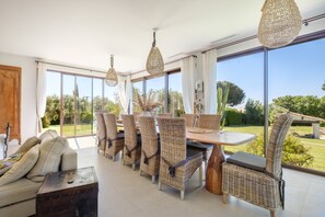 A dining area with wicker chairs, a wooden table, and large windows offering a view of the outdoors. - Le Mas des Serens: A haven of peace with exceptional panoramic views (La Gaude)
