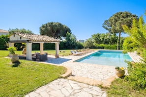 Una piscina con lettini, una pergola e un vialetto in pietra.