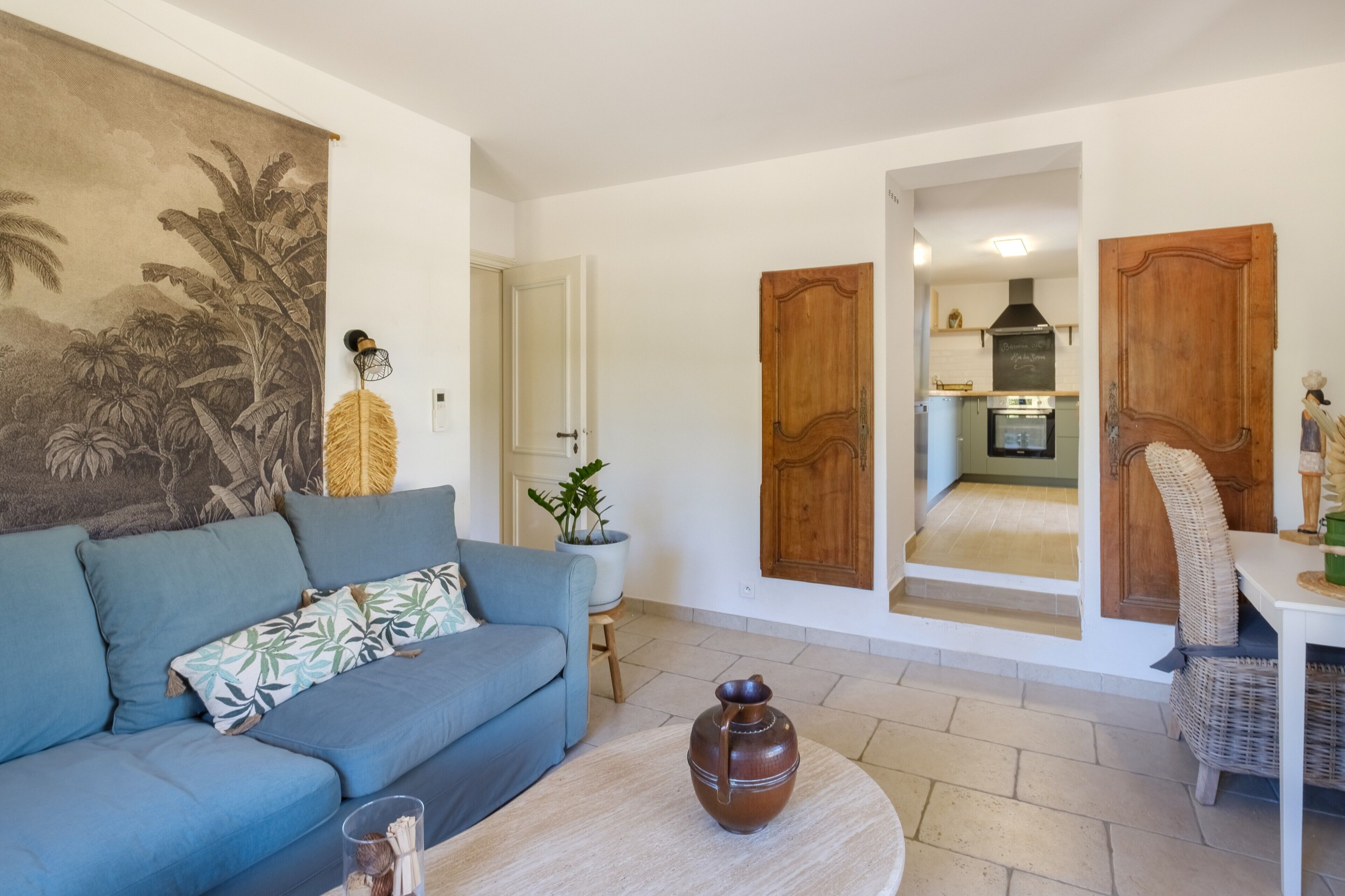 Una sala de estar con un sofá, una mesa de centro, un cuadro y vista a la cocina por una puerta abierta.