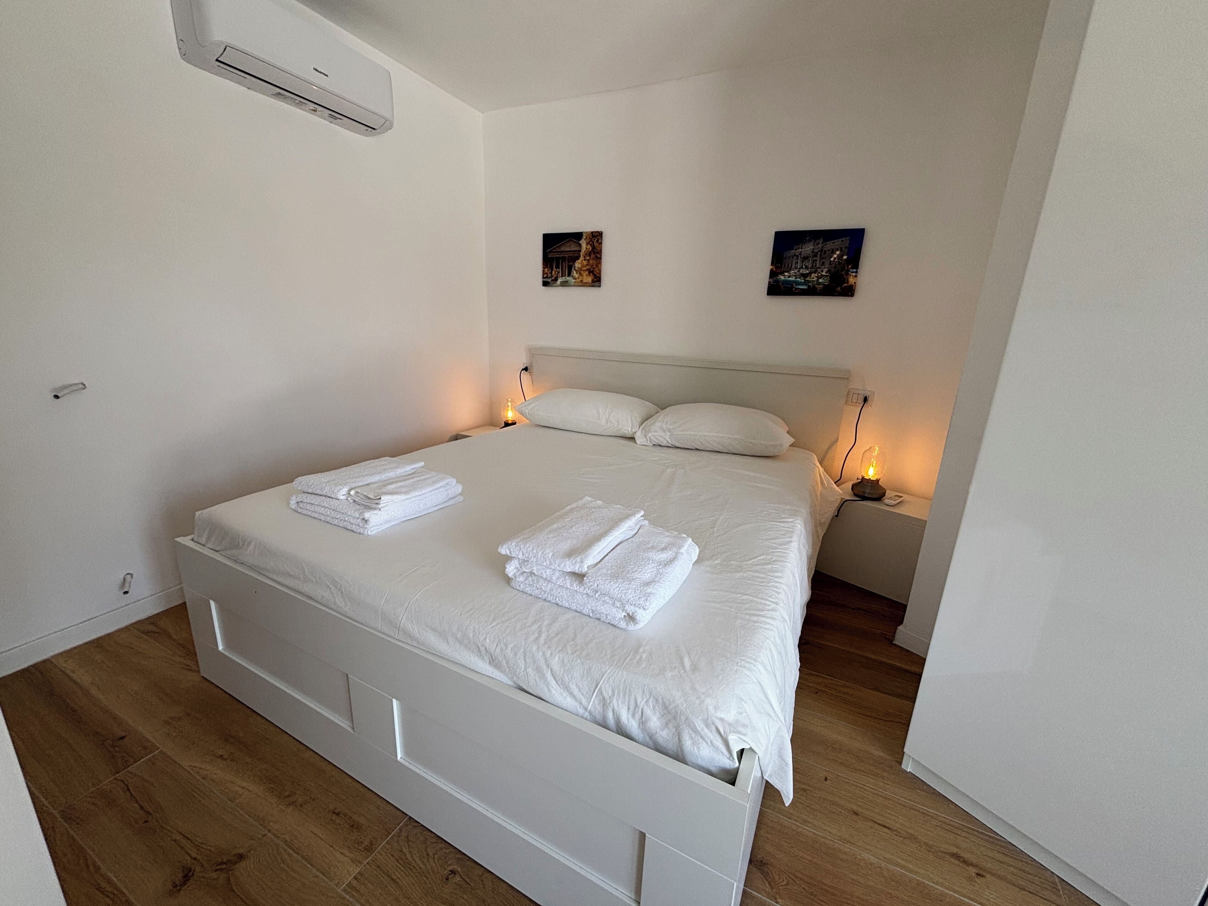 Un lit bien fait, avec du linge de lit et des serviettes blanches, une tête de lit blanche et deux lampes de chevet.