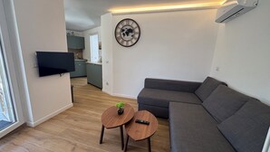 Una sala de estar moderna con un sofá gris, una mesa redonda de madera y un televisor de pantalla plana montado en la pared.