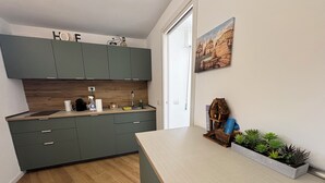 Una cocina moderna con armarios grises, una encimera de madera y un lavamanos pequeño. En la pared, un cuadro de un paisaje urbano, un comedero para pájaros de madera y una maceta con suculentas.