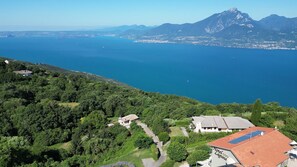 A hotel with a red roof, surrounded by lush greenery and a view of the sea and mountains.