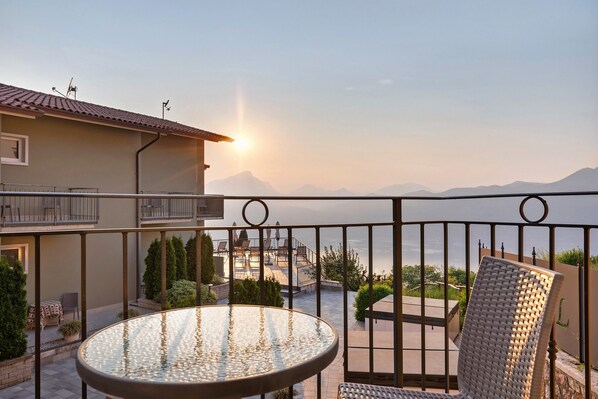 A balcony with a glass table and wicker chair, overlooking a mountainous landscape.