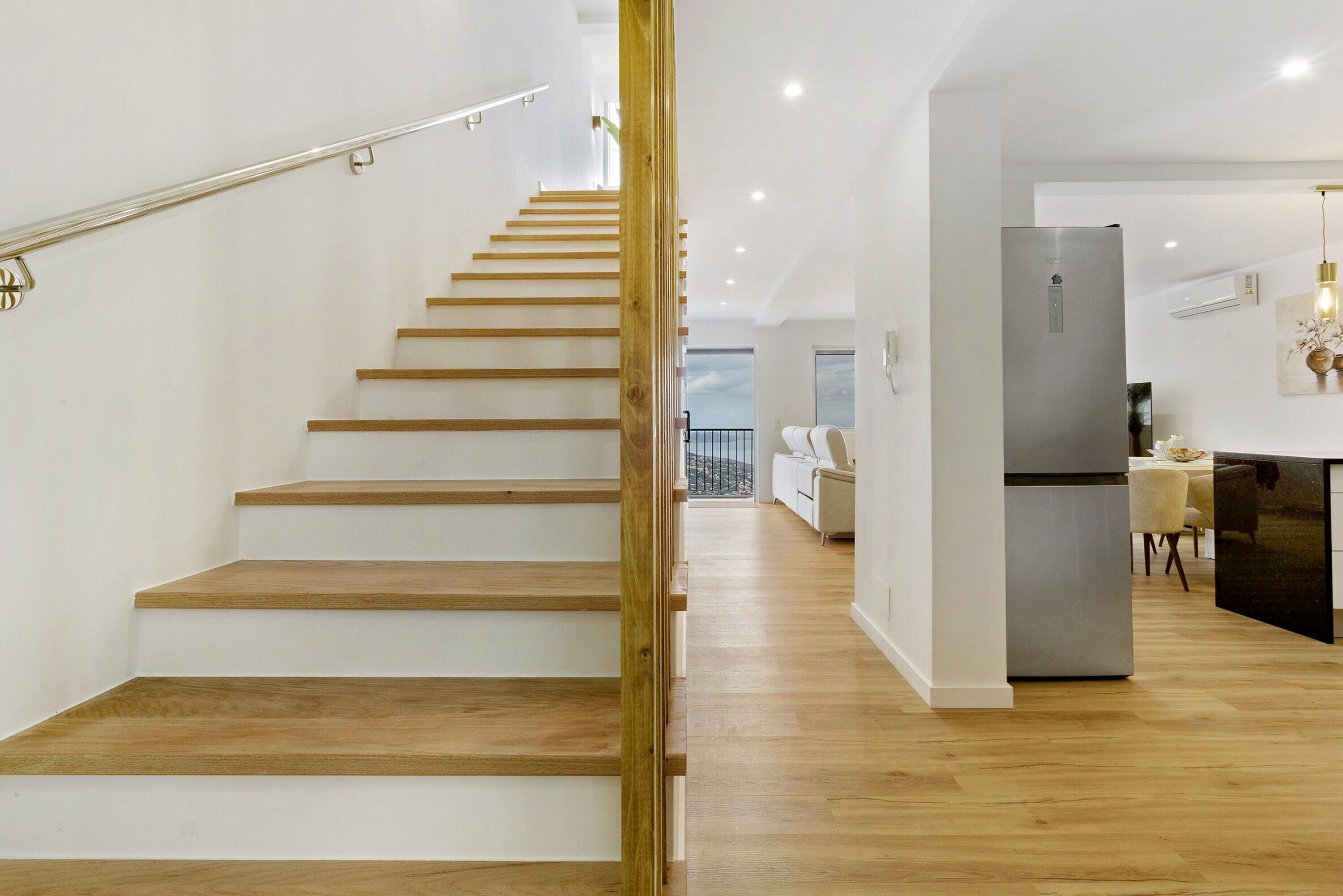 A modern interior with a wooden staircase, a kitchen area, and a dining space.