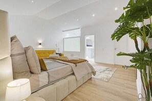 Ein modernes Schlafzimmer mit einem Bett, Nachttisch, Lampe und einer großen Pflanze.