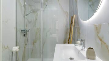 A modern bathroom with a glass-enclosed shower, a white sink with a marble countertop, and a mirror.