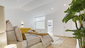 Un dormitorio moderno con cama, mesita de noche, lámpara y una planta grande.