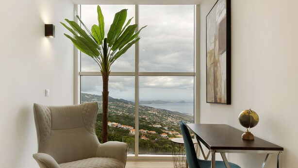 Una habitación moderna con un ventanal grande, un sillón cómodo, una mesa de comedor con sillas, una planta en maceta y un globo terráqueo sobre la mesa.