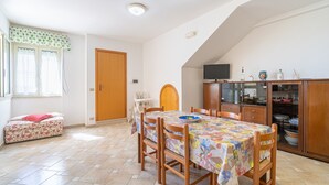 Un coin repas avec une table dressée pour quatre personnes, un canapé, un téléviseur et un meuble contenant de la vaisselle.