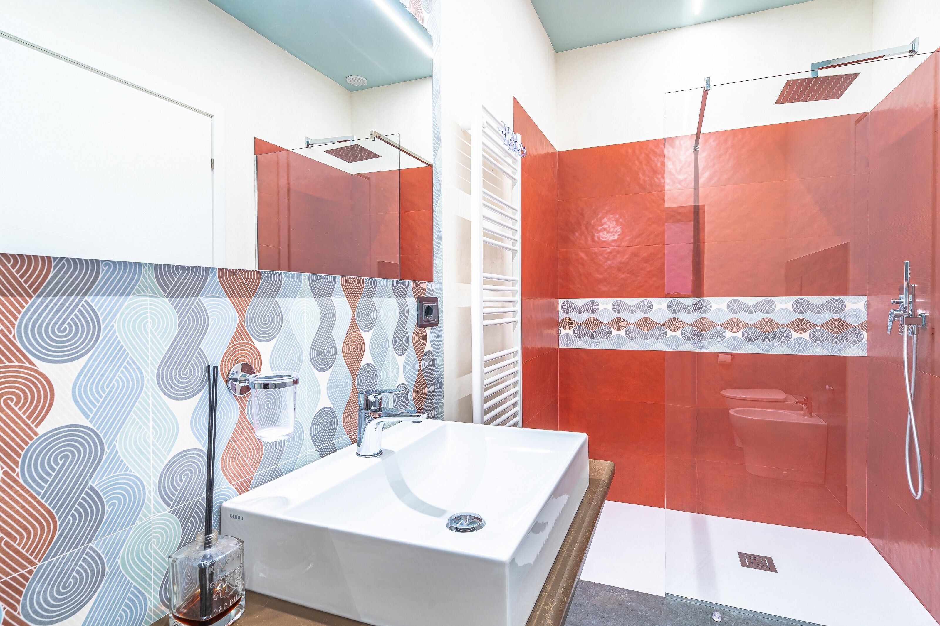 A modern bathroom with a large white sink, a glass shower enclosure, and patterned wall tiles.