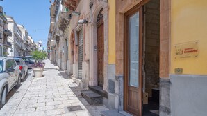 Une rue étroite bordée de voitures garées, un immeuble avec une porte en bois et une enseigne indiquant « 3 Cirnicechi ».