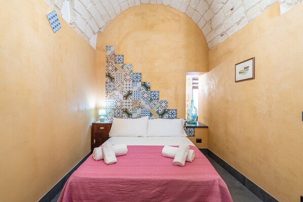 A hotel room with a bed, a nightstand, a tiled wall, and a framed picture on the wall.