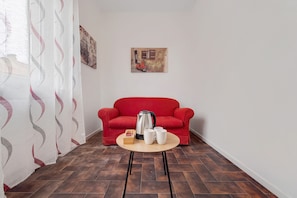 A room with a red sofa, a small round table with a kettle and cups, and a wall with a framed picture.