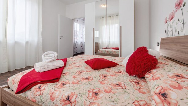 Een slaapkamer met een bloemenbedekking, een rood kussen, een spiegel en een houten hoofdbord.