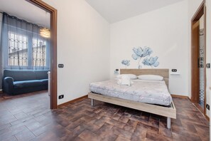 A bedroom with a bed, a window with bars, a hanging light fixture, and a wall with a floral mural.