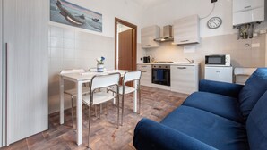A compact kitchen with a dining area, a blue sofa, and a painting on the wall. - Apartment 'Blu' with Shared Terrace and Wi-Fi (Fabbrica Durini)