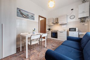A compact kitchen with a dining area, a blue sofa, and a painting on the wall.