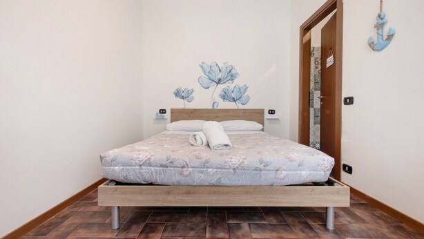 A bedroom with a wooden bed, a floral bedspread, a white towel, and a wall-mounted anchor decoration. - Apartment 'Blu' with Shared Terrace and Wi-Fi (Fabbrica Durini)