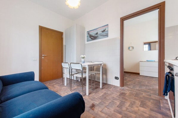 A room with a bed, a dining table with chairs, a kitchen area, and a large mirror.