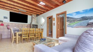 Una sala de estar con sofá, una mesa de centro de vidrio, sillas de madera, chimenea, televisor y un mural de un paisaje.