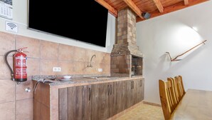 Una cocina con horno de ladrillo, armarios de madera, un extintor y un comedor con mesa y sillas.