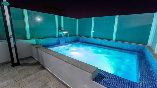 Un jacuzzi con borde de azulejos, un grifo metálico y un panel de control a la izquierda.