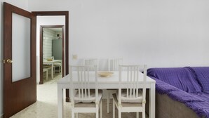 A room with a white dining table, four chairs, a purple blanket on a couch, and a wooden door.