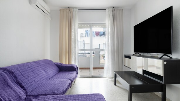 A room with a purple sofa, a flat-screen TV, a sliding glass door, and an air conditioning unit.