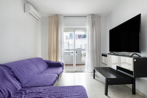 Habitació amb un sofà morat, un televisió de pantalla plana, una porta corredissa de vidre i un aparell d'aire condicionat.