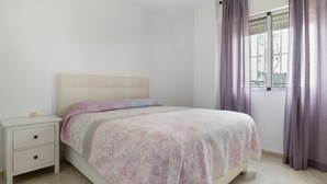A bedroom with a bed, a nightstand, a window with curtains, and a ceiling fan.