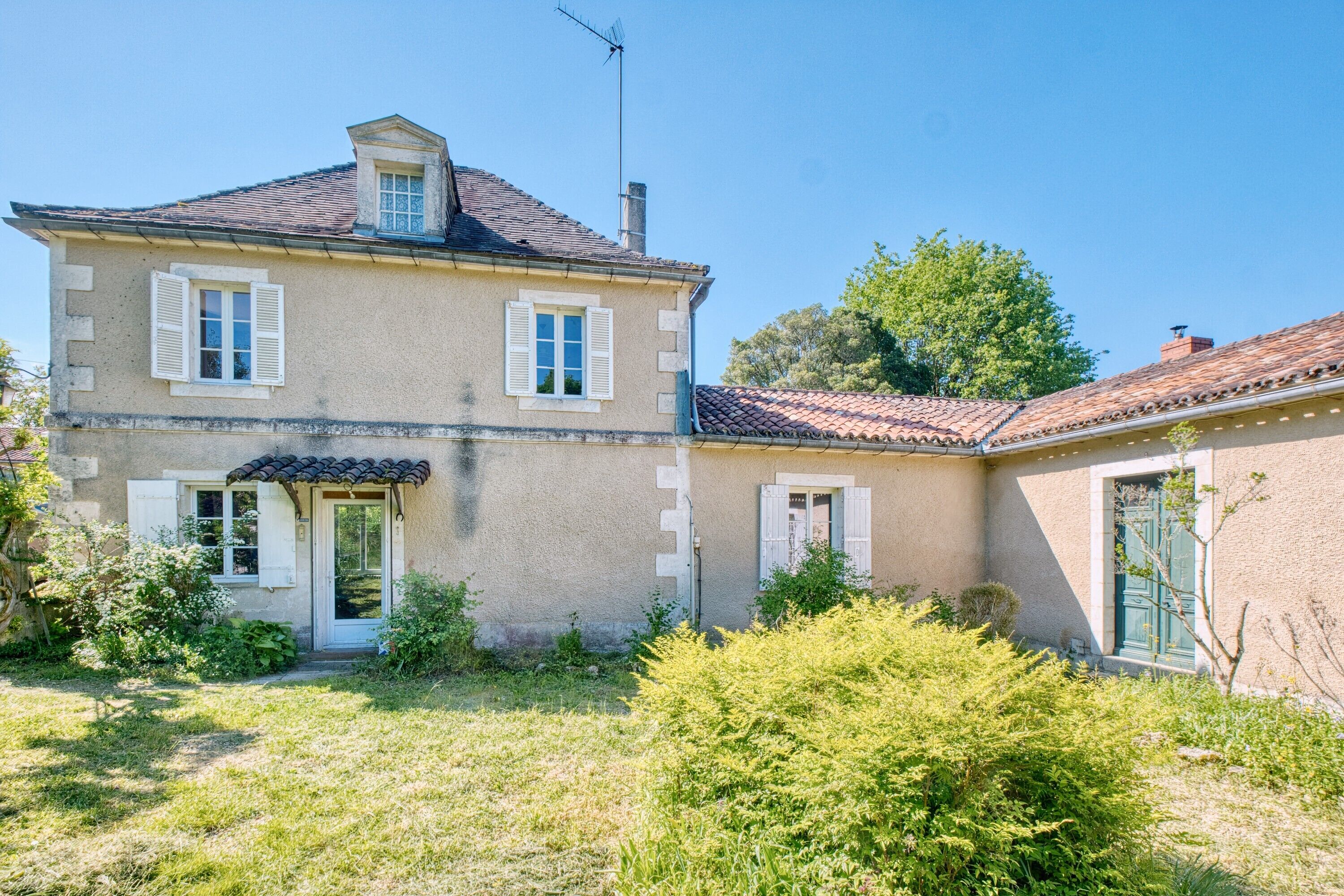 A two-story house with a tiled roof, a small porch, and a garden area.