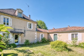 Une maison à deux étages, avec un toit en tuiles, une cheminée et un petit balcon.