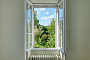 An open window with a view of greenery and trees outside.