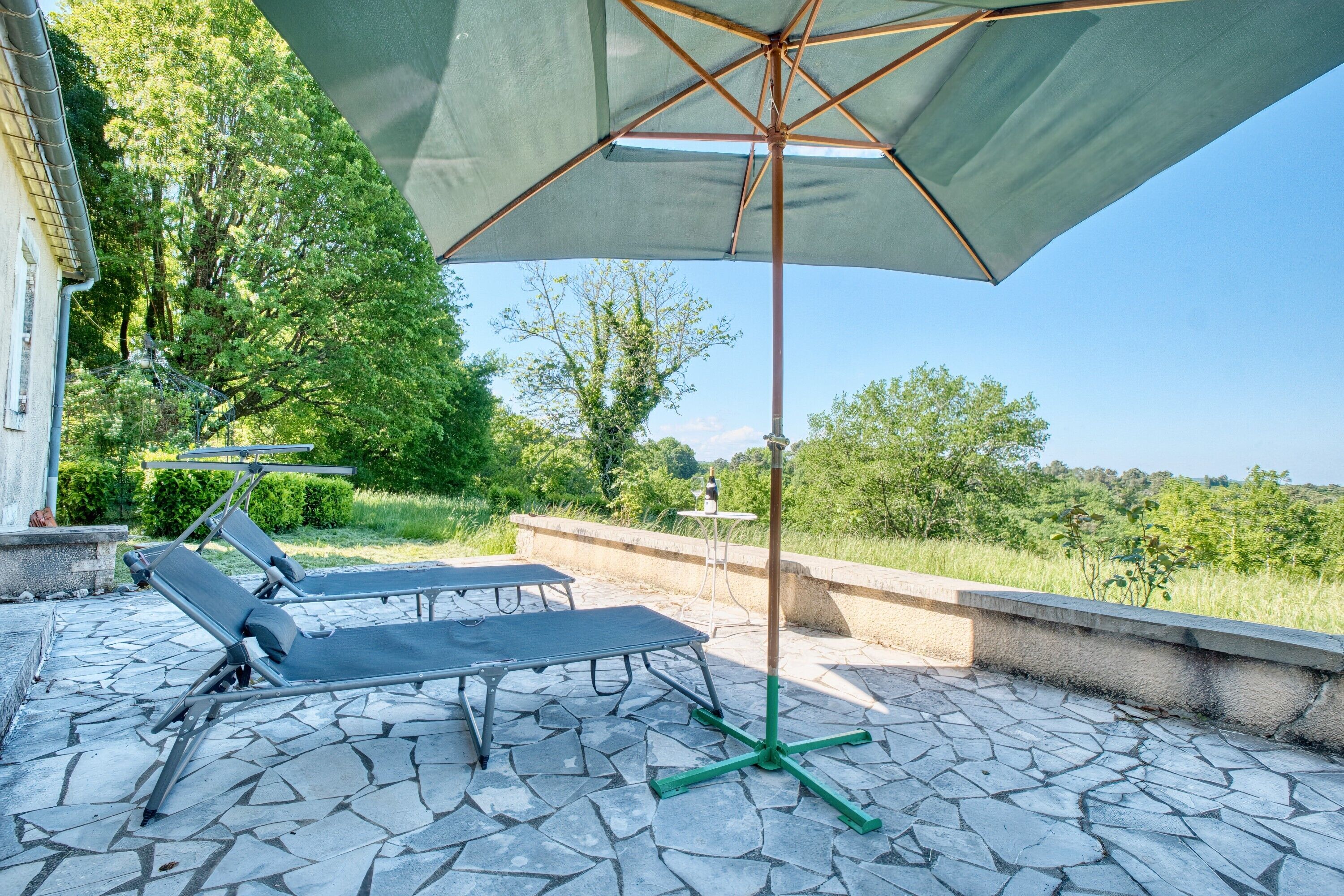 A patio with stone flooring, a green umbrella, and two lounge chairs.