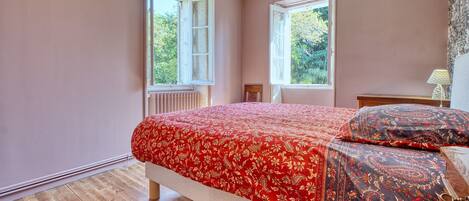 Un dormitorio con cama, dos ventanas, un radiador y una lámpara.